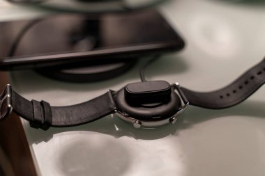 detail of a sports watch charging in focus and a smartphone charging on a wireless charging base.