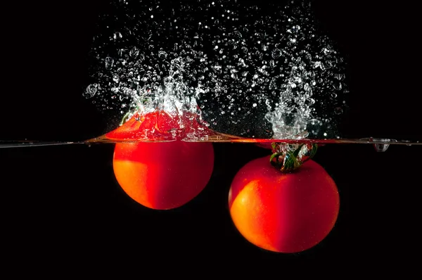 Два помидора падают в воду — стоковое фото