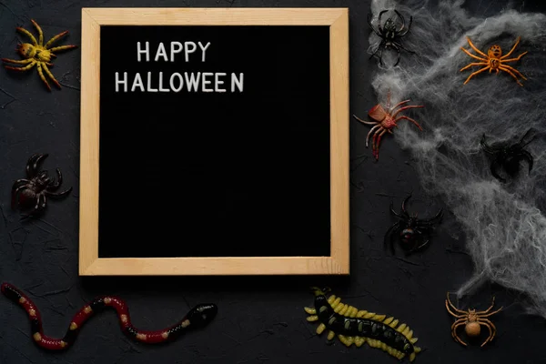 Pókháló, kígyók, cukorkából és lekvárból készült rovarok fekete alapon, Halloween, felülnézet. boldog halloween szöveg — Stock Fotó