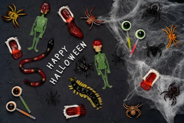 Pókháló, kígyók, cukorkából készült rovarok és lekvár fekete alapon, Halloween, felső nézet — Stock Fotó