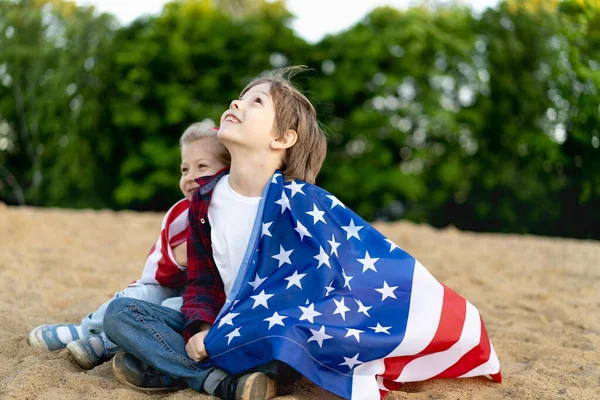 海岸の兄弟姉妹、アメリカの国旗に包まれた幸せな笑いの子供、少女と少年、愛国心の概念と米国の独立のお祝い。退役軍人の日 — ストック写真