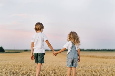 Buğday biçilmiş bir tarlada el ele tutuşan erkek ve kız kardeşler, aile içinde çocukların ilişkisi kavramı..