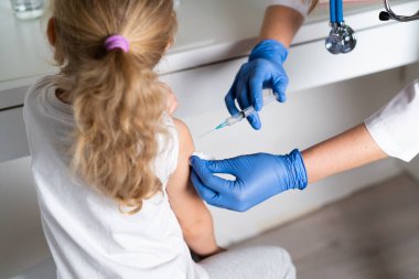 Çocukların aşılanması, doktor randevusundaki küçük bir kız, koluna iğne vurulması,