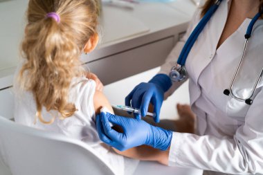 Çocukların aşılanması, doktor randevusundaki küçük bir kız, koluna iğne vurulması,