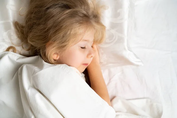 Una rubiecita está durmiendo dulcemente en una cama con ropa interior blanca. espacio para el texto. El sueño sano del niño — Foto de Stock