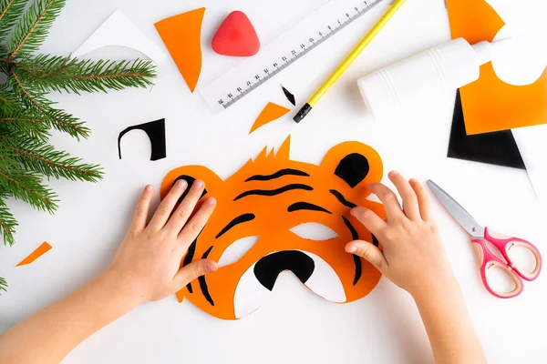 The process of making a childrens New Year tiger mask with a child made of colored paper, top view, symbol 2022, step 6 — Stock Photo, Image