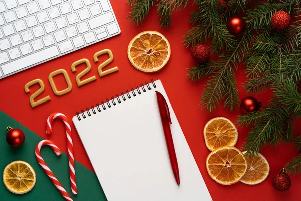 Fondo rojo navideño con ramas y bolas de abeto, bolígrafo y cuaderno con una hoja en blanco para texto, el concepto de planificación 2022 y resumiendo los resultados del año saliente — Foto de Stock