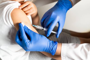 Çocukların aşılanması, doktor randevusundaki küçük bir kız, koluna iğne vurulması, kapalı çekim.