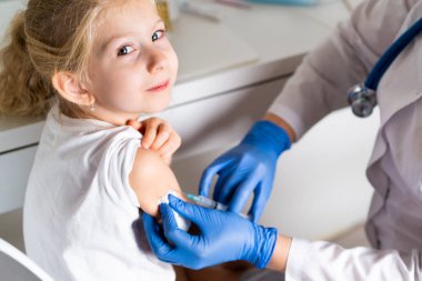 Çocukların aşılanması, doktor randevusundaki küçük bir kız, koluna iğne vurulması,