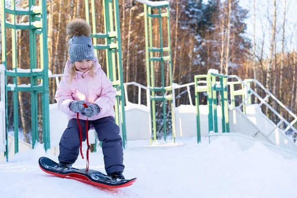 Küçük tatlı kız snowboard yapmayı öğreniyor, çocuklar için kış sporları, aktif sporların güvenliği.