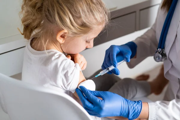 Çocukların aşılanması, doktor randevusundaki küçük bir kız, koluna iğne vurulması,