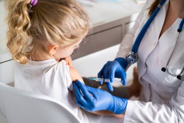 Çocukların aşılanması, doktor randevusundaki küçük bir kız, koluna iğne vurulması,