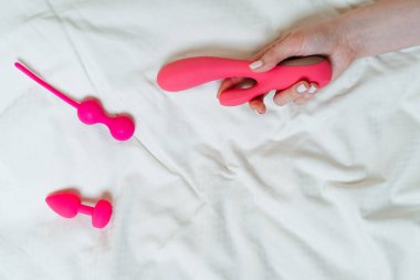 Farklı seks oyuncaklarıyla hafif arka plan. Bir kadının elinde bir vibratör. Ev hanımı konsepti, metin için yer