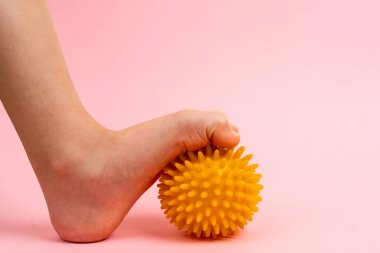 Masaj için sarı iğne topu ve çocuk ayaklı pembe bir arka planda fizik tedavi. Ayak valesinin önlenmesi ve tedavisi kavramı.