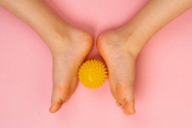 Masaj için sarı iğne topu ve çocuk ayaklı pembe bir arka planda fizik tedavi. Ayak valesinin önlenmesi ve tedavisi kavramı.
