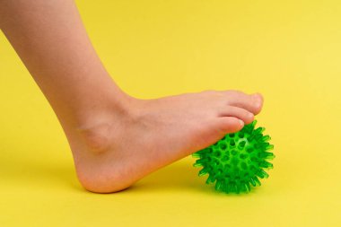 Yeşil iğne topu masaj ve fiziksel terapi için sarı arka planda çocuk ayağı, ayak valesinin önlenmesi ve tedavi konsepti