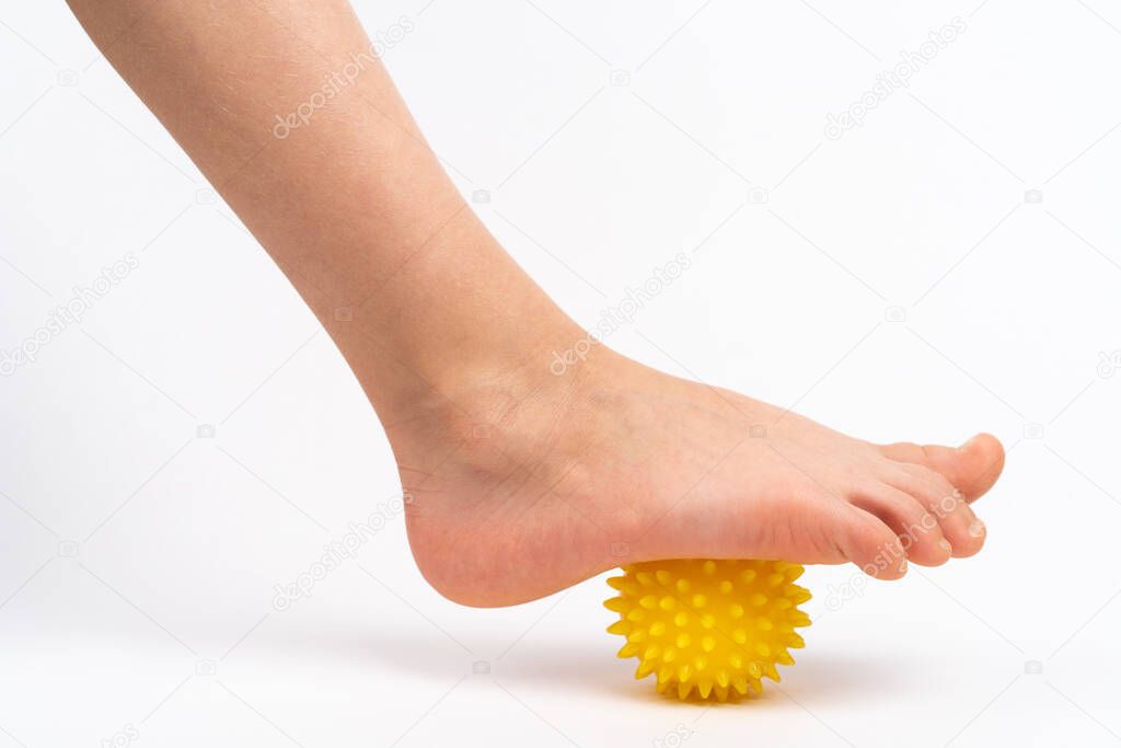 yellow needle ball for massage and physical therapy on a white background with a childs foot, the concept of prevention and treatment of foot valgus