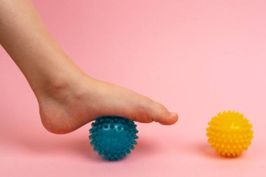Masaj ve fizik tedavi için mavi ve sarı iğne topu. Pembe arka planda çocuk ayağı, ayak kapağının önlenmesi ve tedavi edilmesi kavramı.
