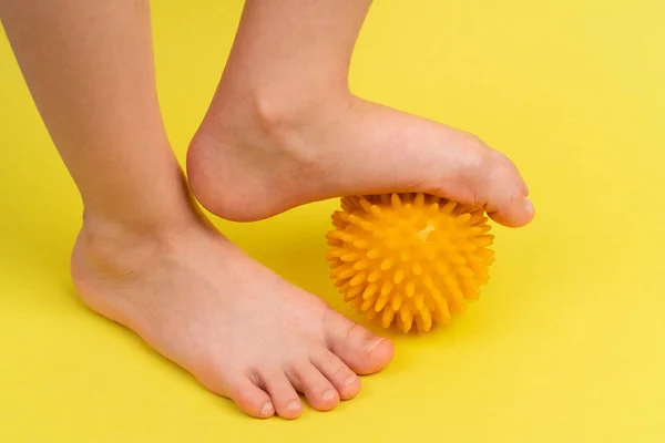 Bola de aguja amarilla para masaje y fisioterapia sobre un fondo amarillo con un pie de niño, el concepto de prevención y tratamiento del valgo del pie Fotos De Stock Sin Royalties Gratis