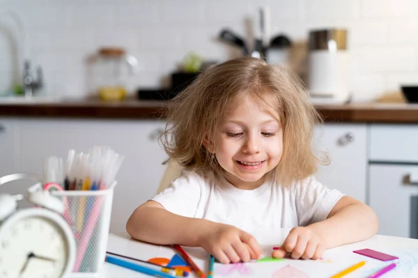 Κουρασμένη μικρή ξανθιά κοπέλα στο σπίτι στο τραπέζι της κουζίνας, η έννοια της εκπαίδευσης στο σπίτι — Φωτογραφία Αρχείου