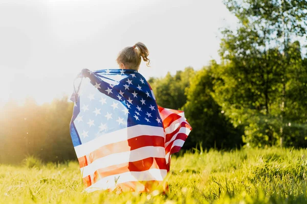 太陽の下で自然の中でアメリカ国旗を持つ美しい小さなブロンドの女の子 — ストック写真