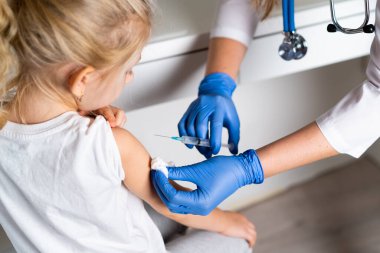 Çocukların aşılanması, doktor randevusundaki küçük bir kız, koluna iğne vurulması,
