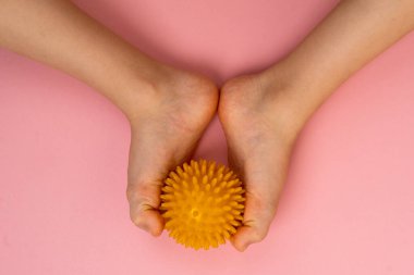 Masaj için sarı iğne topu ve çocuk ayaklı pembe bir arka planda fizik tedavi. Ayak valesinin önlenmesi ve tedavisi kavramı.