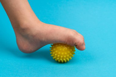 Masaj için sarı iğne topu ve çocuk ayağı olan mavi arka planda fizik tedavi, ayak valesinin önlenmesi ve tedavi konsepti.