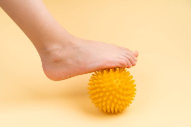 Masaj için sarı iğne topu ve bej bir arka planda fizyoterapi. Üzerinde çocuk ayağı resmi var. Hallux valgus önleme ve tedavi kavramı.