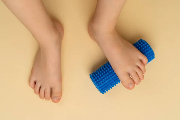 Bej bir arka planda masaj ve fizyoterapi için mavi iğne silindiri. Üzerinde çocuk ayağı resmi var. Hallux valgus önleme ve tedavi kavramı.