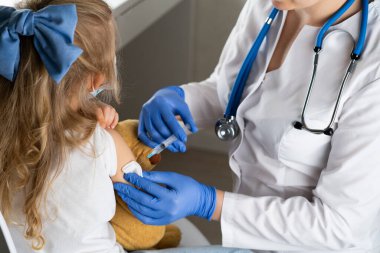 Çocukların aşılanması, doktor randevusundaki küçük bir kız, koluna iğne vurulması,.