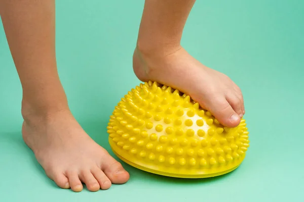 Niños pies con un equilibrador amarillo sobre un fondo verde claro, tratamiento y prevención de pies planos, deformidad valgus del pie Imagen De Stock