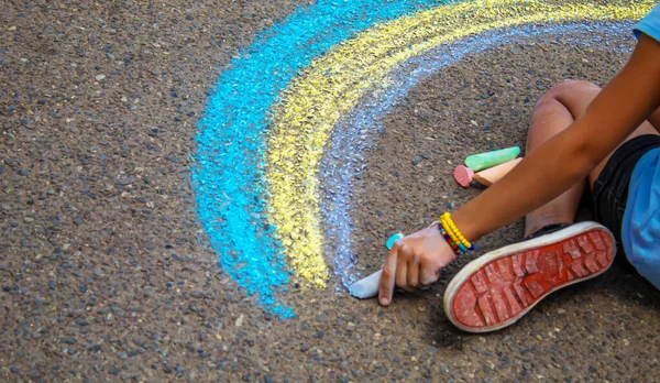 A child draws a rainbow on the asphalt. Selective focus. kid.