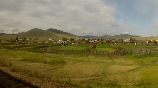 Tren pasando por un pequeño pueblo en un verde paisaje siberiano — Vídeos de Stock