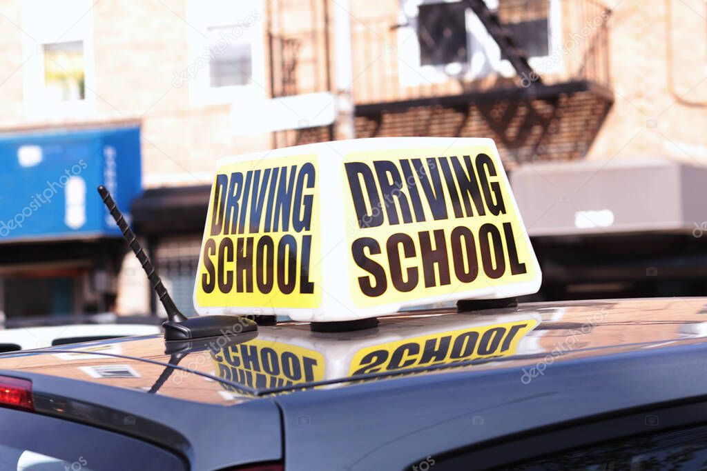 Close up of large driving school sign on the roof of a practice car in a busy city street