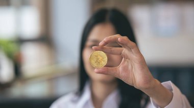 Genç Asyalı kadın gülümsüyor, Bitcoin kriptosu tutuyor. Bitcoin olarak dijital paraya para yatıran Asyalı bir kadın. Genç tüccar ya da yatırımcı Kripto para birimiyle ilgileniyor.