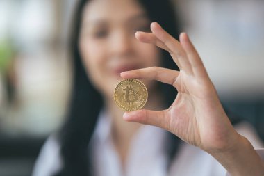 Genç Asyalı kadın gülümsüyor, Bitcoin kriptosu tutuyor. Bitcoin olarak dijital paraya para yatıran Asyalı bir kadın. Genç tüccar ya da yatırımcı Kripto para birimiyle ilgileniyor.