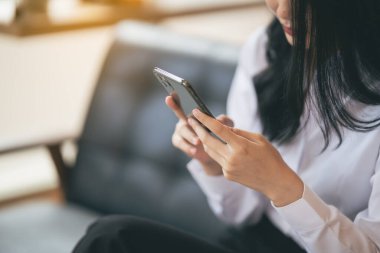 Genç Asyalı bir kadın bir kafede akıllı telefondan mesaj yazıyor. Genç bir kadının kahve masasında cep telefonu kullanırken çekilmiş görüntüsü..