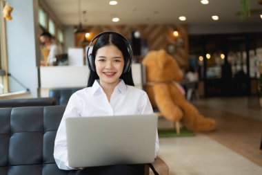 Kafede otururken bilgisayarla gülümseyen mutlu Asyalı kadın. Genç Asyalı bir kadın bir kafede oturuyor ve bilgisayar başında video konferansı düzenliyor..