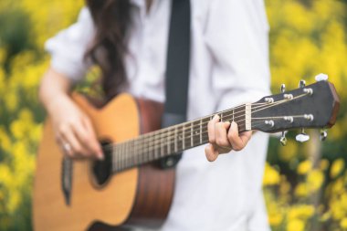 Parkta gitar çalıp şarkı söyleyen Asyalı genç bir kadın, sarı çiçek bahçesinde gitar çalan Asyalı bir kadın.
