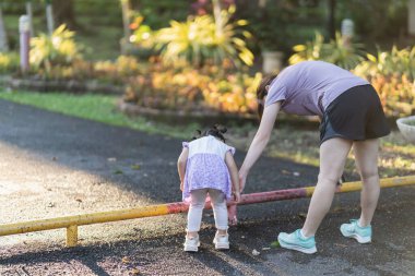 Asyalı anne ve kızı parkta koşmaya gitmeden önce bacaklarını esnetiyorlar. Küçük kız arkadan görüldü. Anne ve kızı spor kıyafeti giyiyorlar..