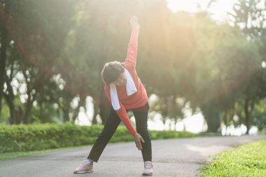 Kıdemli Asyalı kadın vücudu egzersiz yapmadan önce ısınıyor. Bahçede koşmadan önce esneme hareketleri yapan yaşlı kadın, spor koşucusu konsepti..