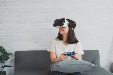 Asyalı kadın evde eğlenmek için video oyunu oynuyor, Asyalı kadın tatilde evde neşeli. Mutlu kadın metaverse VR teknoloji konsepti oynuyor.