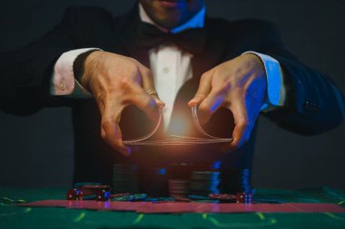 Adam satıcı ya da krupiye, elinde iki iskambil kâğıdı olan bir kumarhanenin arka planındaki poker kartlarını karıştırıyor. Kumarhane, poker, poker konsepti