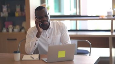Kafe masasında cep telefonuyla konuşan Afrikalı işadamı, cep telefonuyla konuşan dizüstü bilgisayarlı ve uzaktan kumandalı bir girişimci..