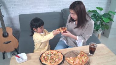 Asyalı anneler ve çocuklar evde faaliyet gösteriyor. Anne çocukları için pizza besleyecek. Çocuklar İtalyan ev yapımı pizza yiyor ve tadıyorlar. Şirin çocuklar rahat evlerinde lezzetli yemekler yiyorlar.