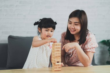 Jenga oyunları konsepti. Asyalı kız ve anne mutlu bir şekilde gülümsüyor ve gülüyor. Oturma odasındaki kanepede oturup ahşap Jenga oyunları oynuyorlar. Anne ve kız aile aktiviteleri mutlu oyunlar oynuyor.