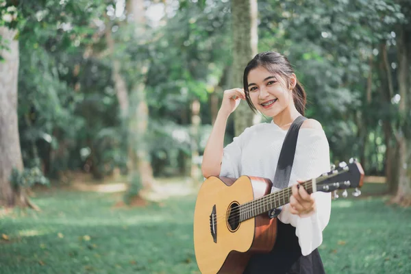 アジアの若い女性がギターを演奏し 公園で音楽を歌う アジアの女性が庭でギターを演奏 — ストック写真