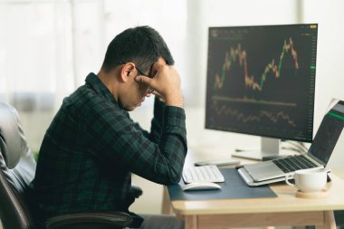 Asyalı tüccar mutsuz ve ciddi bir şekilde merkez ofiste kripto döviz grafiğiyle monitörlerin önünde oturmuş elinde akıllı telefon izleme kripto para birimi fiyatı tutuyordu.