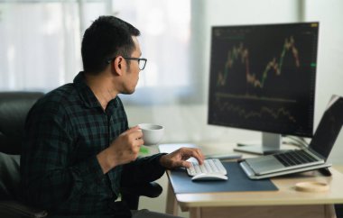 Kahve içen Asyalı tüccar şifreli döviz grafiğiyle monitörlerin önünde oturmuş elinde akıllı telefon izleme kripto para birimi fiyatı tutuyordu.